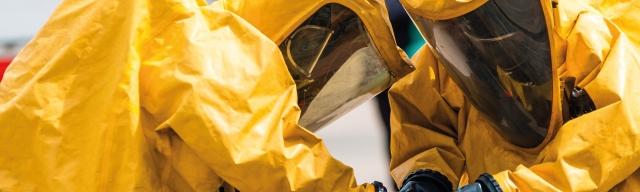 Two workers in PPE handling bin of hazardous waste