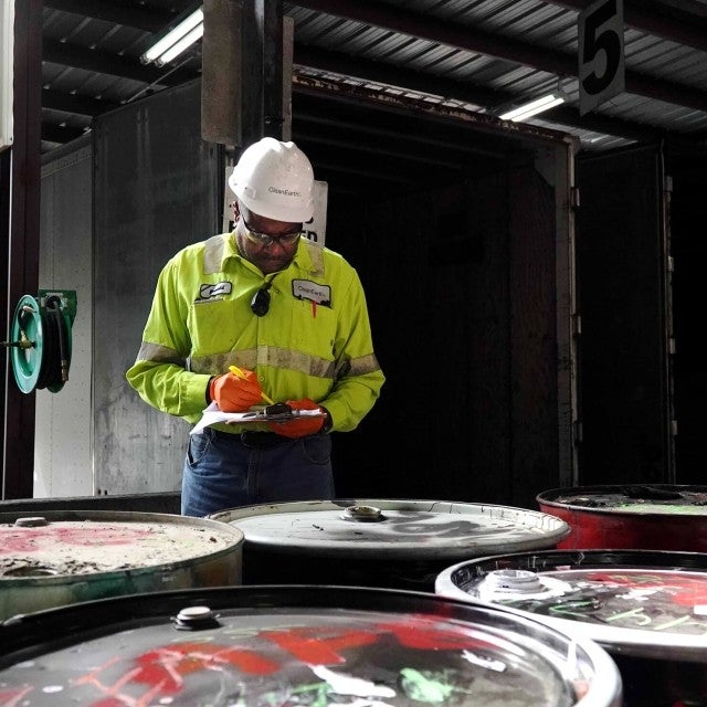 man in PPE inspecting barrels of hazardous waste