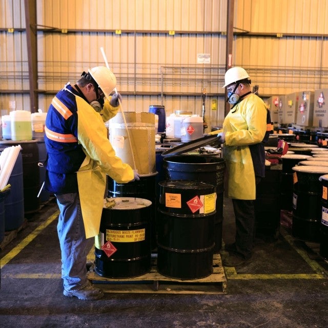 Two people in PPE sampling materials from barrels 