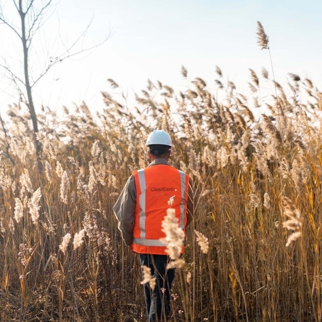 man in high visibility vest walking through reeds 