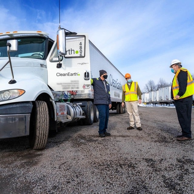 Three people standing by semi truck talking 