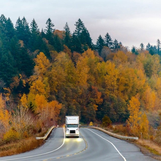 semi-truck driving on road through autumn forest 