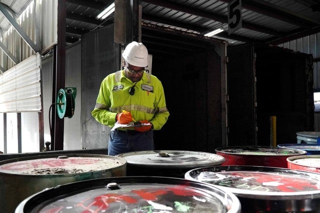 man in PPE inspecting barrels of hazardous waste