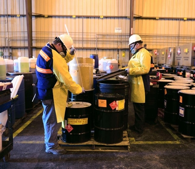 Two people in PPE sampling materials from barrels 