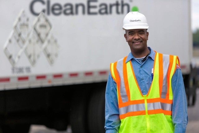 man in safety vest and hard hat smiling in front of truck