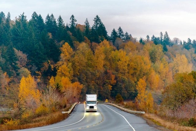 semi-truck driving on road through autumn forest